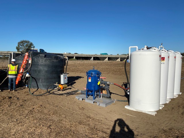 A field jobsite with a black frac tank, blue bag filters and white Pure Effect carbon vessels, with a worker in a safety vest