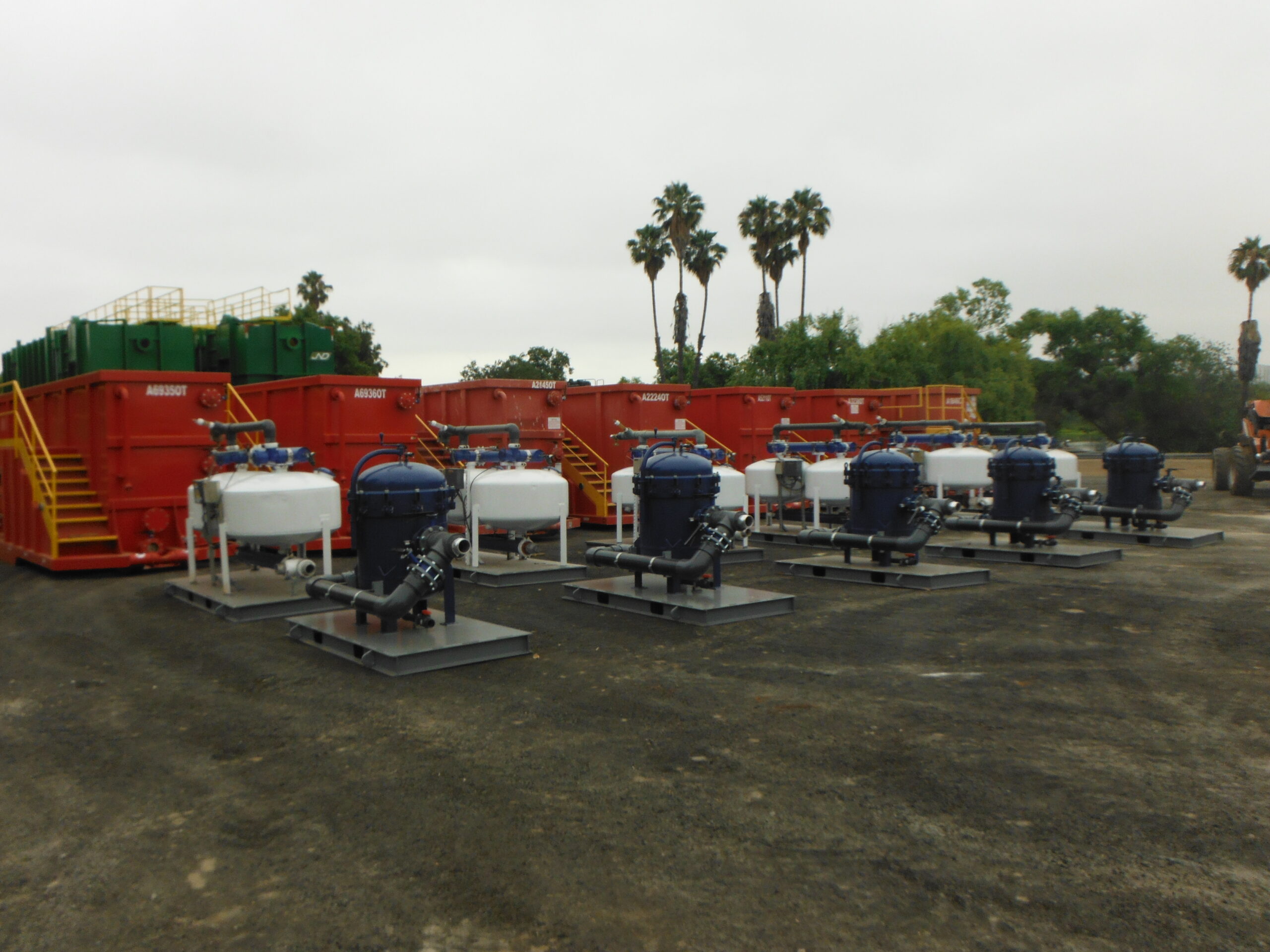A fleet of blue Pure Effect sand and carbon filtration units staged in front of red frac tanks at the equipment yard