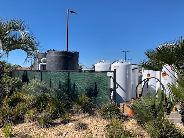 A black poly tank and white Pure Effect carbon vessels set behind a screened jobsite fence with palm landscaping