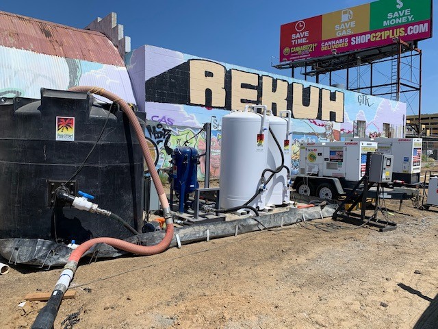 A black tank and white Pure Effect carbon vessels with generators at a fenced urban dewatering jobsite in front of a mural