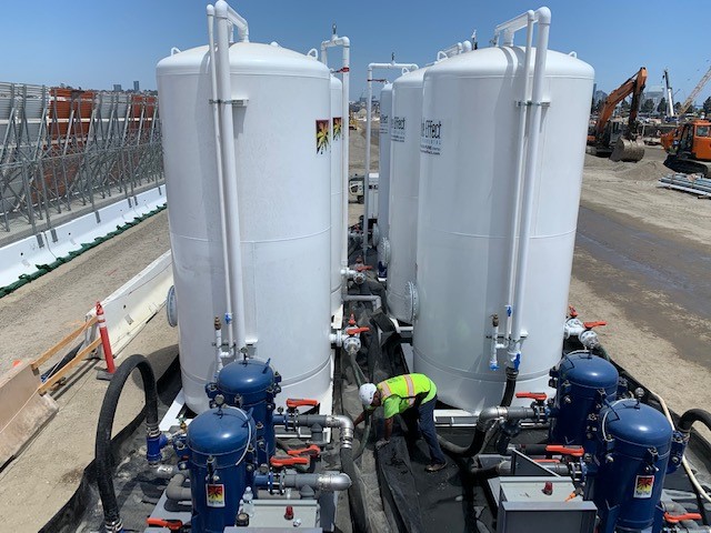 Two white Pure Effect carbon vessels over blue bag filters with a worker in a hard hat at an elevated urban jobsite