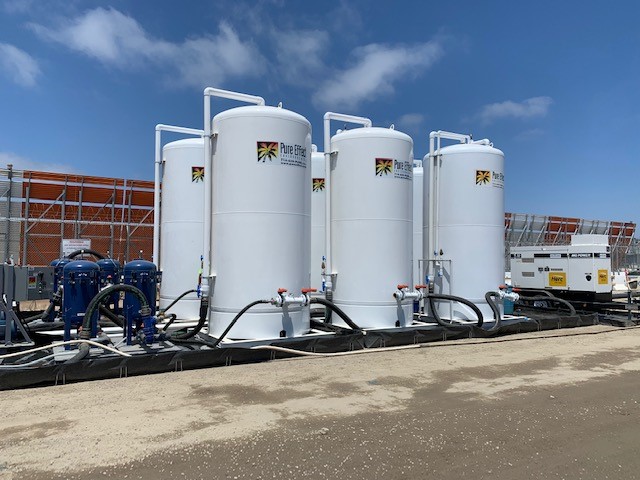 Three branded white Pure Effect carbon vessels over blue bag filters set on a black containment liner at a fenced jobsite