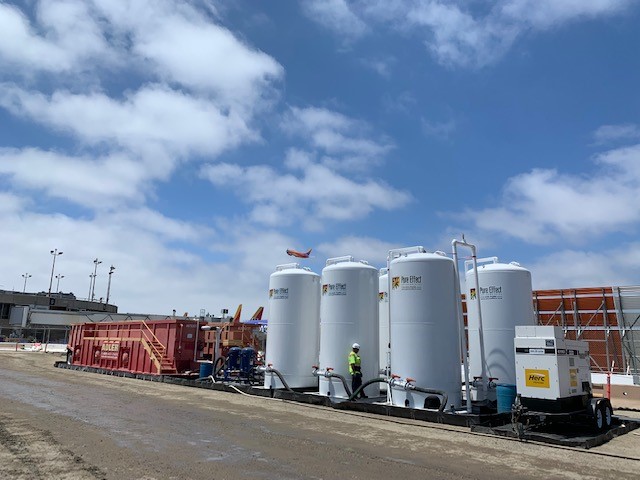 A long row of branded white Pure Effect treatment tanks and vessels lined up behind a chain-link fence at a San Diego dewatering job
