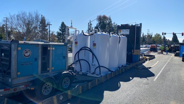 White Pure Effect water-treatment vessels loaded on a flatbed trailer with a generator at a street-side jobsite