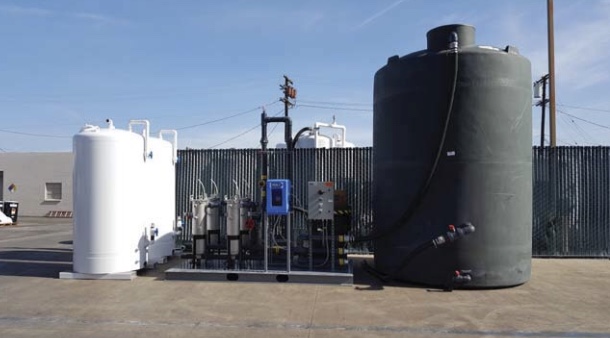 A white Pure Effect carbon vessel with skid-mounted filters beside a large black poly tank at a fenced equipment yard