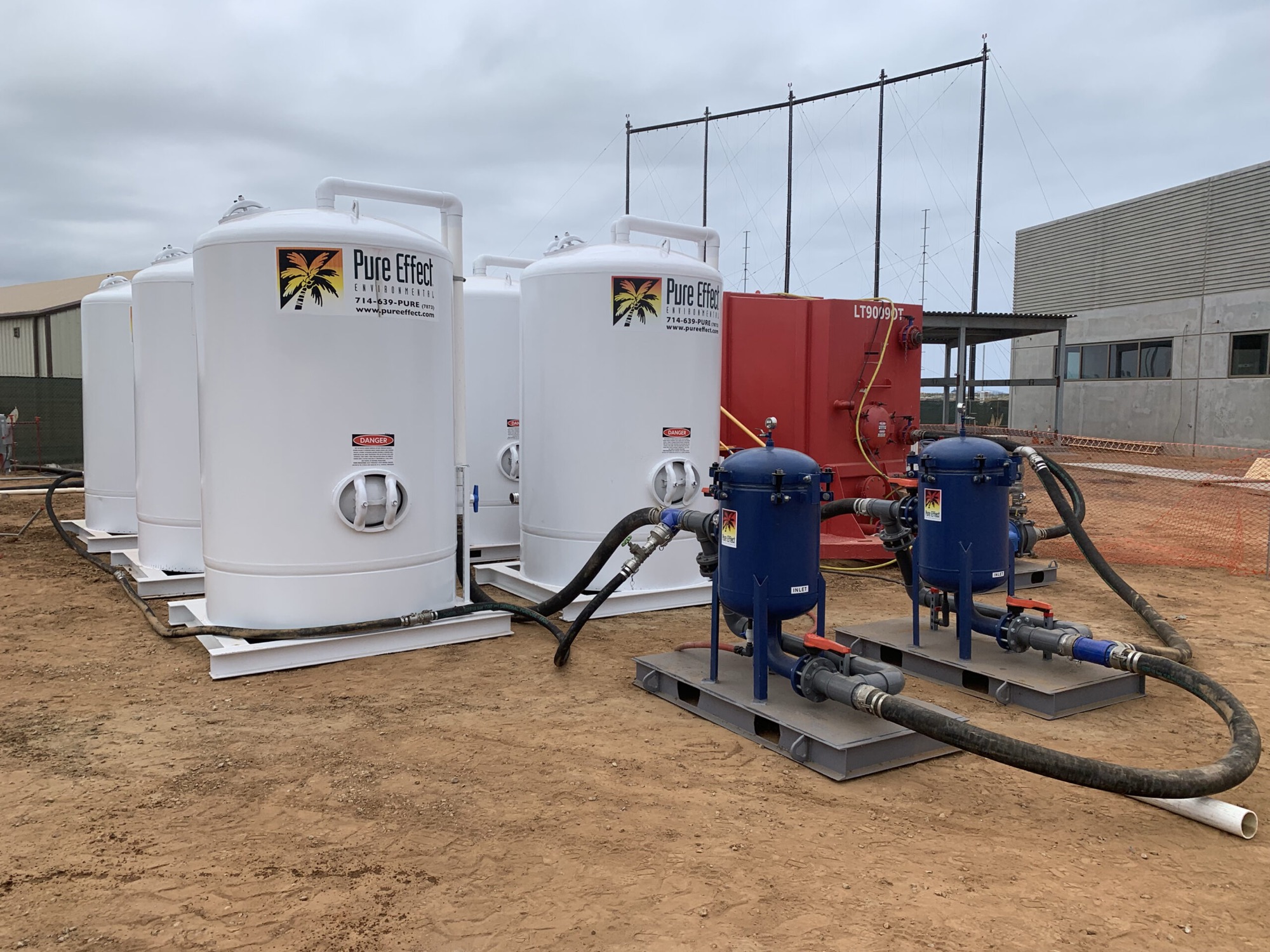 Branded white Pure Effect carbon vessels and blue bag filters plumbed together with a red frac tank at a construction dewatering jobsite