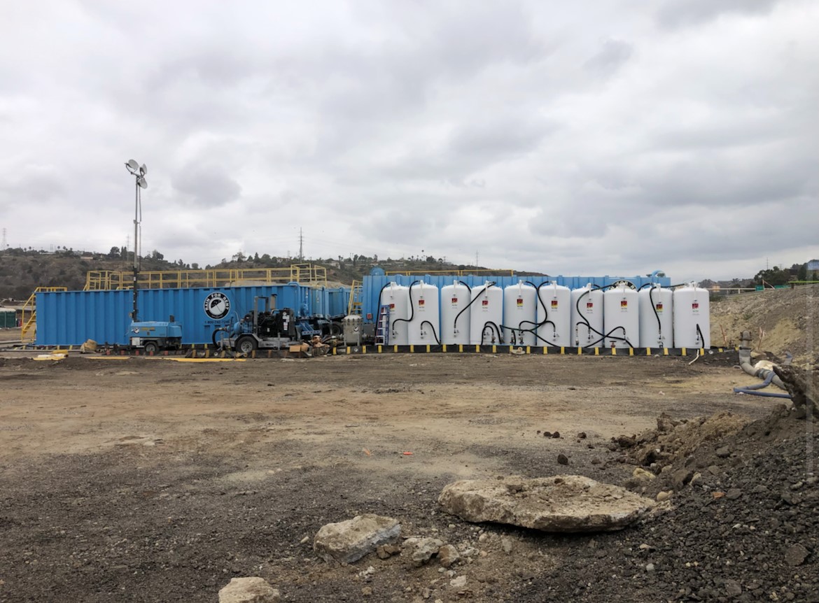 A blue frac tank and a long row of white and blue Pure Effect treatment tanks staged at a large construction dewatering site
