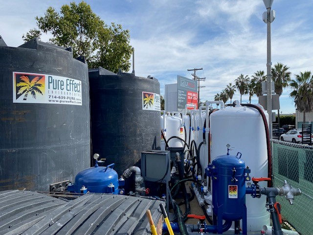 Pure Effect branded black poly tanks with white carbon vessels and blue bag filters set up along a fenced street-side jobsite at Venice Beach