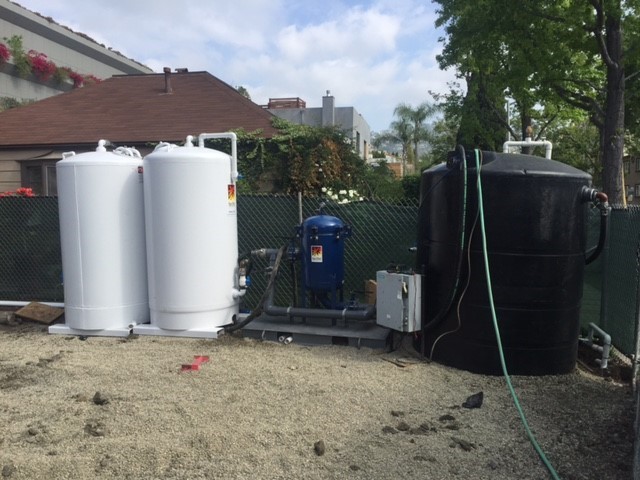 Two white Pure Effect carbon vessels, a blue bag filter and a black holding tank installed on gravel in a residential backyard