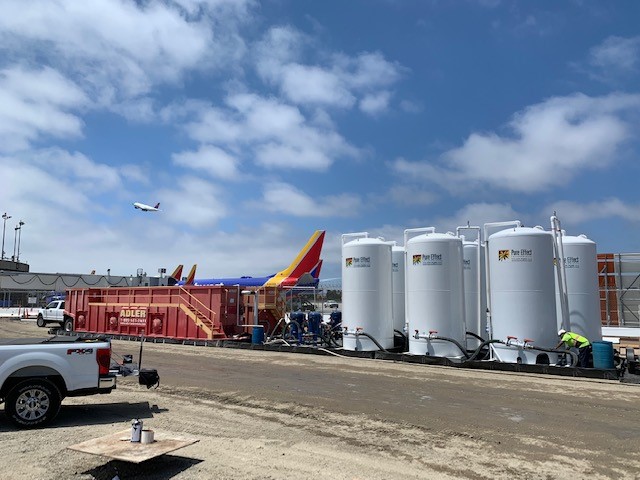 Three white Pure Effect carbon vessels and a red frac tank staged on an airport-area tarmac jobsite